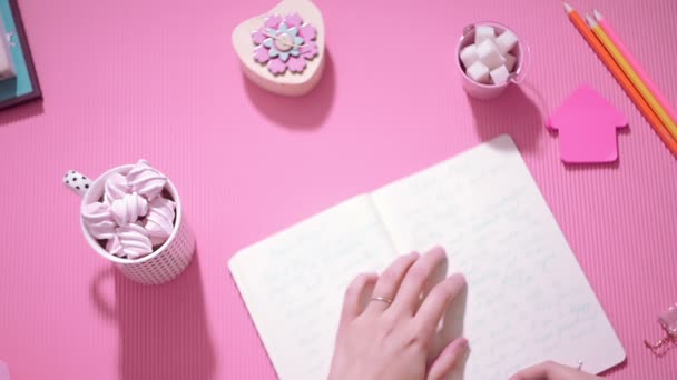 Top view tyttö kirjoittaa päiväkirjaa ja ottaa kupin kaakaota vaahtokarkilla — kuvapankkivideo