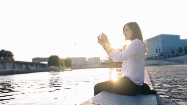 Beautiful girl taking a photo on smartphone sitting near the river middle shot — Stock Video