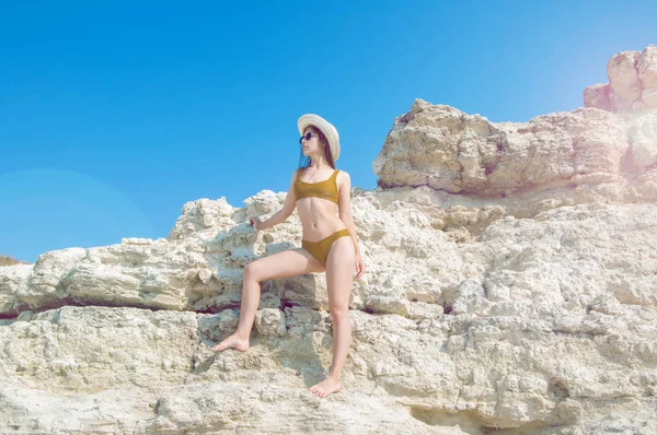 Bir bikini, şapka ve güneş gözlüğü beyaz kayalar arka plan üzerinde güneşlenme güzel kız