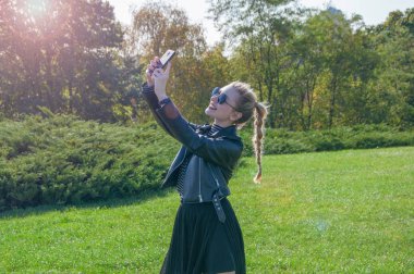 Güzel sarışın kız bir yeşil çim zemin üzerinde duruyor ve selfie yapar