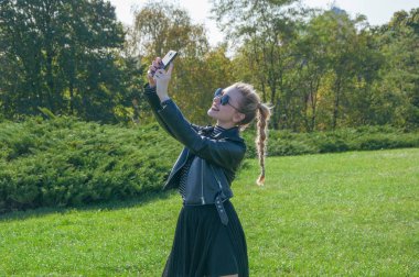 Güzel sarışın kız bir yeşil çim zemin üzerinde duruyor ve selfie yapar