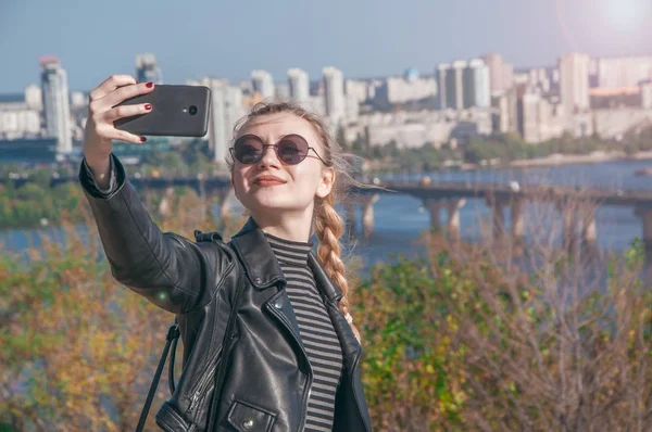 Hermosa chica rubia se para en el fondo de la ciudad y hace selfie — Foto de Stock