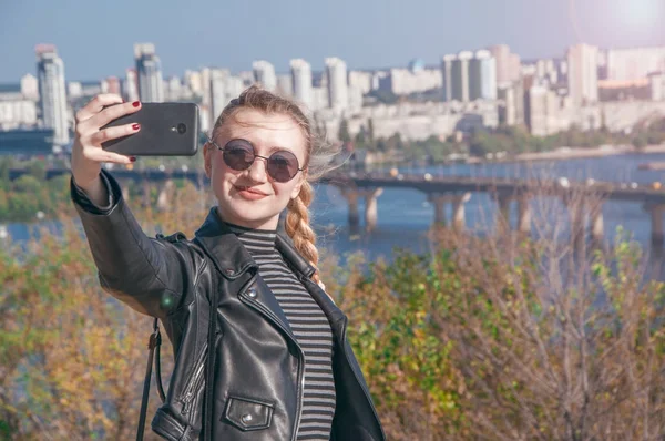 Hermosa chica rubia se para en el fondo de la ciudad y hace selfie — Foto de Stock