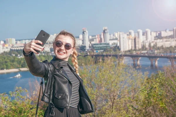 Hermosa chica rubia se para en el fondo de la ciudad y hace selfie — Foto de Stock