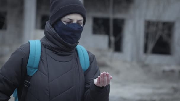 Young woman in a protective mask sprays antiseptic on her hands against the background of an abandoned building in an industrial post-apocalyptic landscape. Pandemic protection, cleaning hands — Stock Video