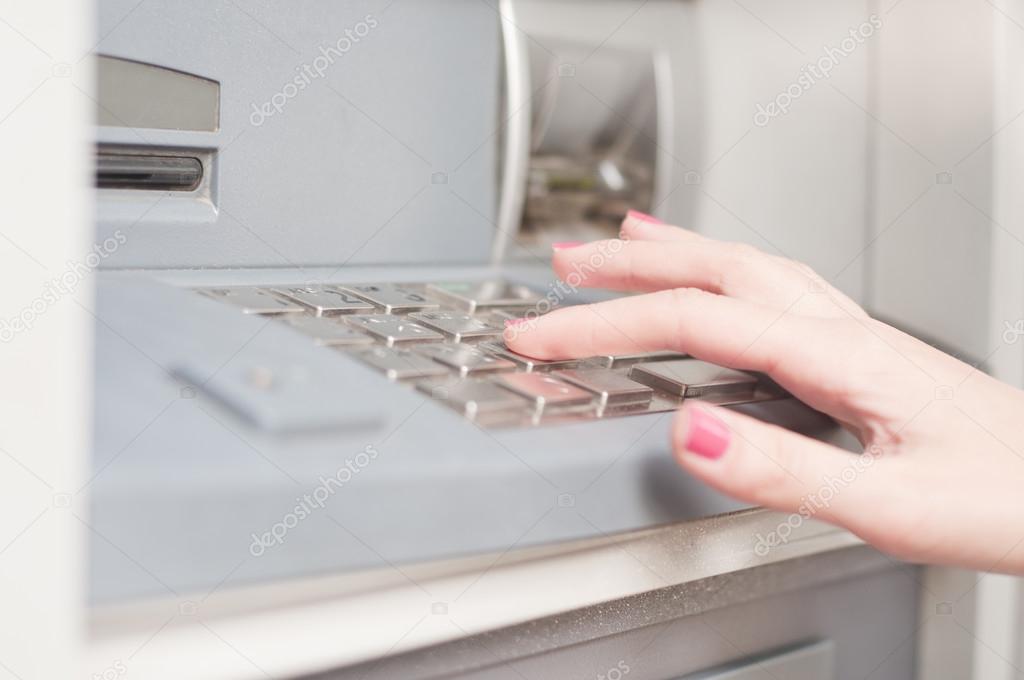 Woman using banking machine. Close up. Finger pressing password number on ATM machine.