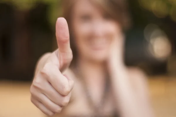 Young women giving thumb up as sign of success.