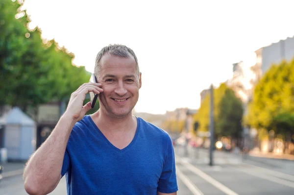 Gelukkig lachend veertig jaar oude Kaukasische toeristische man praten op een mobiele telefoon buiten. — Stockfoto