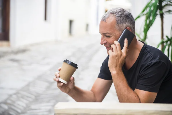 幸せなビジネスマンが携帯電話で話しています。青年実業家が紙コップを押しながら携帯電話経由で通信します。仕事に行くながらスマート フォンで男を笑顔. — ストック写真