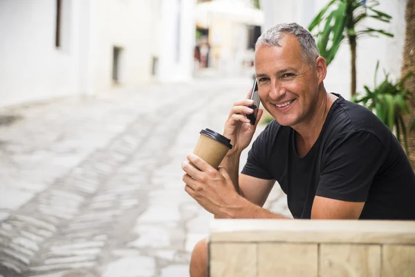 Business man in the city making a phone call with smartphone holding to go cup of coffee or tea