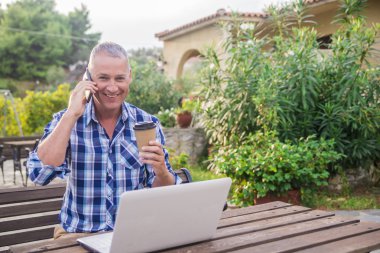 Çekici bir adam içinde senin ev bahçe. çalışma / genç adam çalışma açık havada akıllı telefon ile konuşurken.