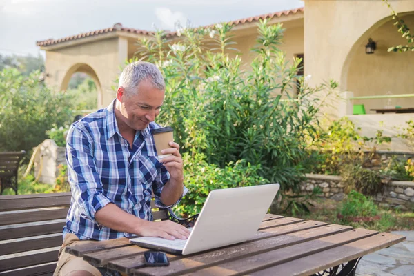 Elegante knappe man met behulp van een laptop en zoeken naar informatie op lijn en koffie drinken — Stockfoto