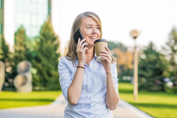 Hermosa mujer mensajes de texto en un teléfono inteligente en un parque con un fondo verde — Foto de Stock