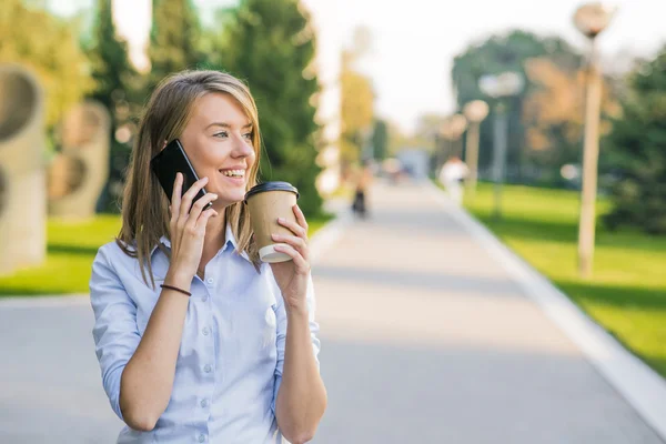 Hermosa mujer mensajes de texto en un teléfono inteligente en un parque con un fondo verde — Foto de Stock