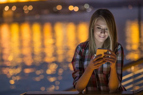 Красивая молодая девушка, использующая смартфон в городе ночью — стоковое фото