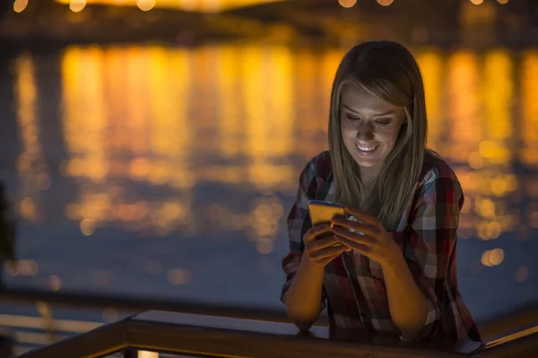 woman using smartphone in city at night. Woman sending text message on phone