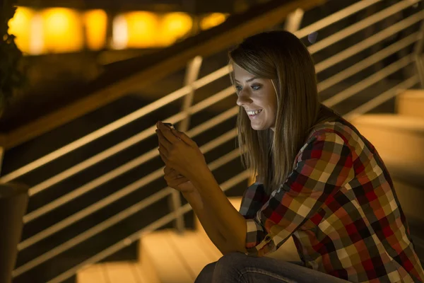 Модная женщина в городе ночью с помощью текстового приложения на смартфоне — стоковое фото