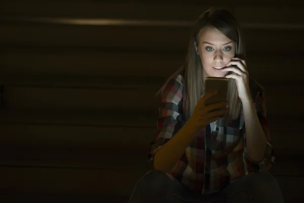 Gyönyörű fiatal nő, női kaukázusi hallgató olvasó szöveges üzeneteket a mobiltelefon tükröződik a lány arc képernyőn könnyű, üres képernyő telefon mobiltelefon éjszakai utcán szabadban, állva — Stock Fotó