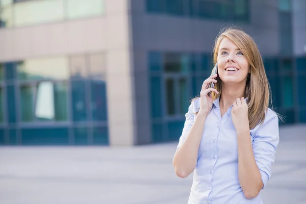 Una joven mujer de negocios hablando por teléfono mientras está de pie frente a un bloque de oficinas — Foto de Stock