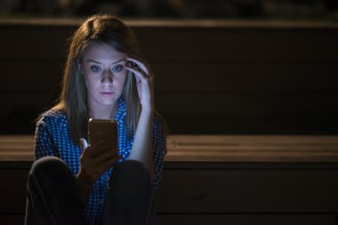 Portre yan görünüm portre genç üzücü düşünceli kadının karşı sokak lambası geceleri bokeh kopya alan arka plan üzerine eğilerek, genç kadın ile hareket eden telefon mesajı okur..