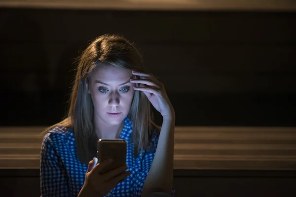 Tråkiga nyheter. Upprörd ung kvinna med mobiltelefon läser meddelandet. Nattporträtt i parken — Stockfoto