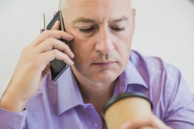 akıllı telefonda konuşurken ve kahve fincanı için seyir sinirli olgun iş adamı