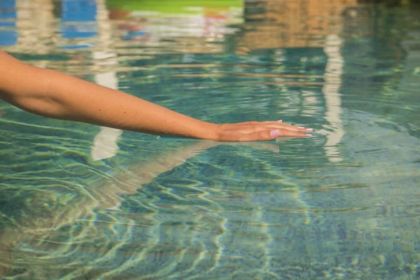 Mujer joven arrodillada junto al borde de una piscina, tocando el agua tranquila con la mano . — Foto de Stock