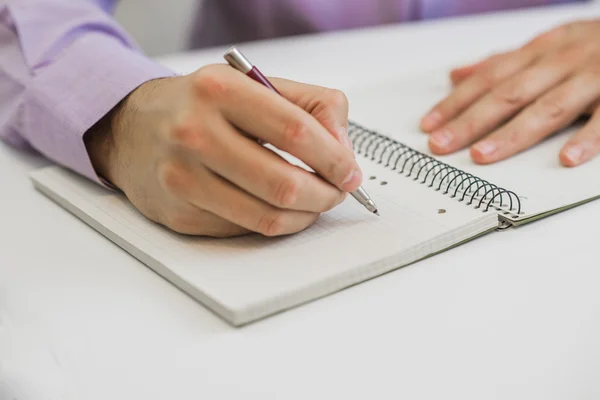 Großaufnahme Geschäftsmann sitzt am Tisch im Bürointerieur und schreibt aufmerksam ein paar Notizen in ein grünes Notizbuch — Stockfoto