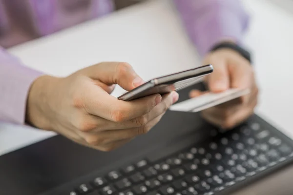 Handen met slimme telefoon en een creditcard, laptop gebruikt. Online winkelen — Stockfoto