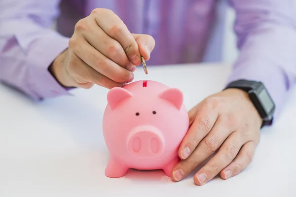 Vista da vicino della mano di un uomo che mette una moneta nello slot di un salvadanaio in un concetto di risparmio e investimento — Foto Stock