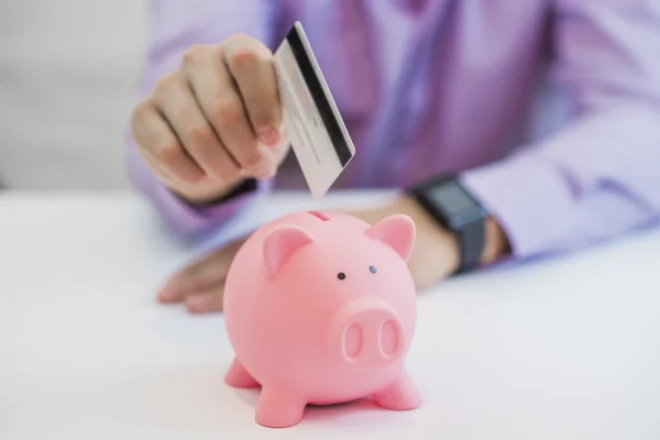 Экономия денег, бизнесмен держит копилку и кредитную карту — стоковое фото