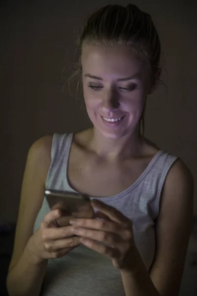 Улыбающаяся девушка с помощью смартфона ночью — стоковое фото