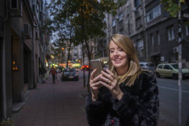 Kadın manifatura. SMS gönderme mobil cep telefonu okumakta Closeup genç mutlu gülümseyen neşeli güzel kadın kız cityscape açık arka plan izole. Pozitif yüz ifade insan duygu