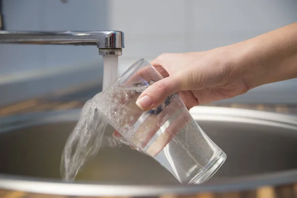 La mano de la mujer llena el vaso de agua . — Foto de Stock