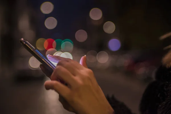 Sokakta cep telefonunu kullanan bir kadın, gece lambası arka planı.