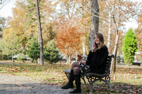 公園のベンチに座りながらスマート フォンを使用して魅力的な少女 — ストック写真