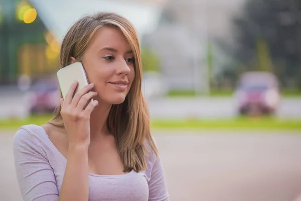 Happy young woman with smartphone standing in the street — Stock Photo, Image