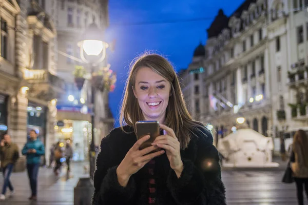 Female using her mobile phone, city skyline night light background. Portrait of a beautiful girl. gorgeous brunette girl, portrait in night city lights. Beautiful girl texting with smart phone