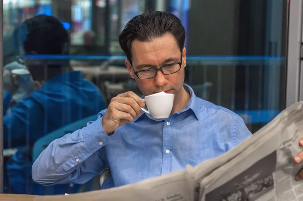 Giovane uomo d'affari che sorseggia caffe 'e legge giornali al caffe'. Uomo d'affari maschile, moderno edificio per uffici con bella luce come sfondo. Uomo d'affari che legge un giornale con una tazza di caffè . — Foto Stock
