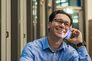 Modern akıllı telefon, onun ofisinde çalışan ve cep telefonu tutan genç mutlu adam kullanarak gülümseyen bir işadamı yakın çekim