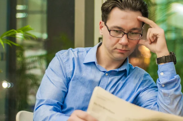 Ritratto di un giovane bell'uomo d'affari che legge un giornale a colazione in una caffetteria, uomo d'affari bruno che tiene aperto un giornale seduto in un bar — Foto Stock