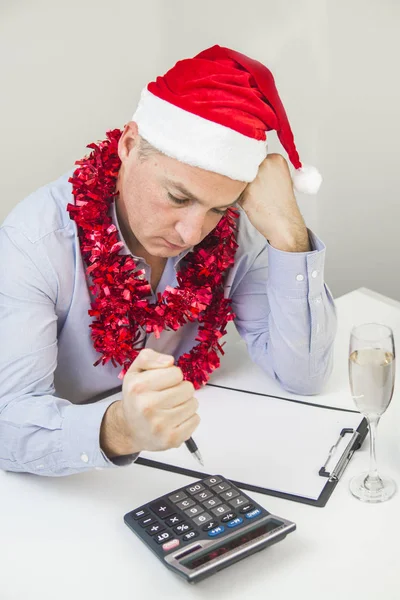 Me siento enfermo y cansado. Joven frustrado manteniendo los ojos cerrados mientras estaba sentado en su lugar de trabajo en la oficina. Hombre de Negocios Celebre Feliz Navidad y Feliz Año Nuevo Use Sombrero de Santa — Foto de Stock