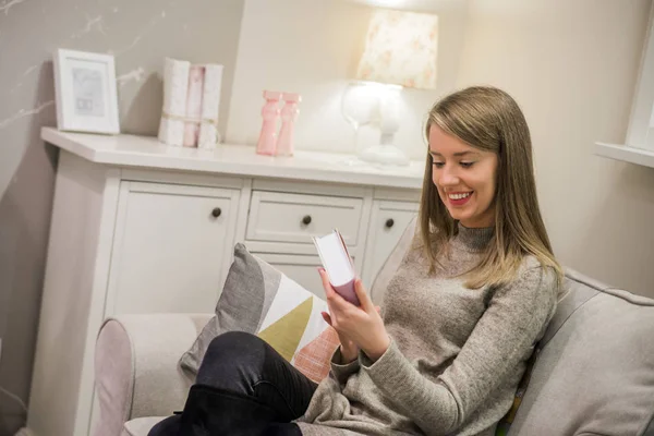 Женщина сидит на диване и читает книгу в гостиной у себя дома. Счастливая молодая женщина читает сказки на диване дома — стоковое фото