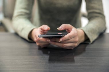 İş kadını ofiste onun masasında telefonunu kullanarak görünümünü kapatın. Ahşap masa üzerinde bir dokunmatik ekran smartphone kullanan kadın