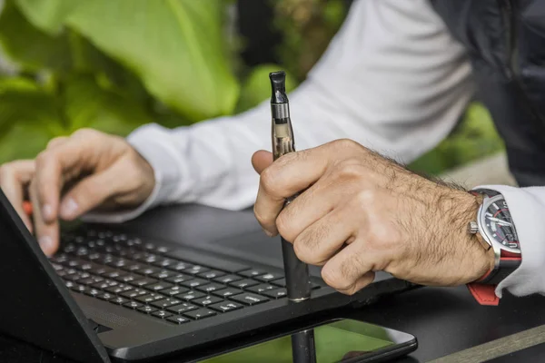 Cropped image of modern man with laptop and e-cigarette. Modern  man sitting in cafe and drinking coffee.