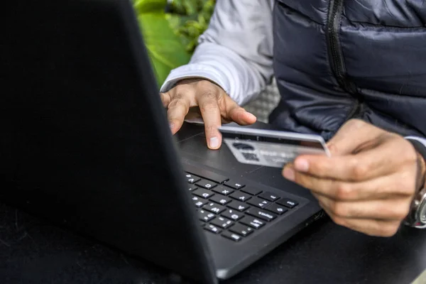 Man holding credit card in hand and entering security code using laptop keyboard. Young businessman holding a credit card and typing. On-line shopping on the internet using a laptop
