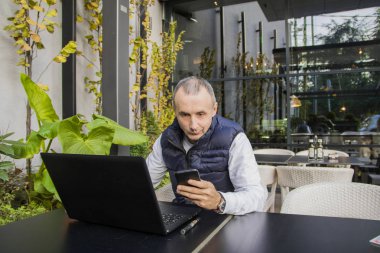 Onun smartphone okunurken gülümseyen genç mutlu bir iş adamı. İş adamı okuma mesaj smartphone Office ile gülümseyen portresi. Çalışan adam. akıllı telefon ve laptop internet kullanarak iş adamı