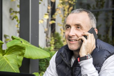 akıllı telefonundan arama yapma ve kafe Teras, açık havada masadan iken bir dizüstü bilgisayar kullanarak verimli işadamı.