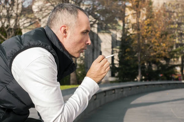 Un tânăr om de afaceri stând lângă un copac într-un parc, relaxându-se cu o țigară. Un om de afaceri bine îmbrăcat fumând pe trotuarul străzii, abuzul de substanțe, dependența, oamenii și conceptul de obiceiuri proaste - aproape de un tânăr fumând țigări în aer liber — Fotografie, imagine de stoc