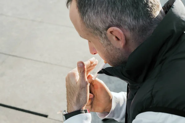 Ein Mann zündet sich draußen eine Zigarette an. Im Mittelpunkt steht die Zigarette. gutaussehender Mann zündet sich Zigarette auf der städtischen Straße an. Stadtmode. — Stockfoto